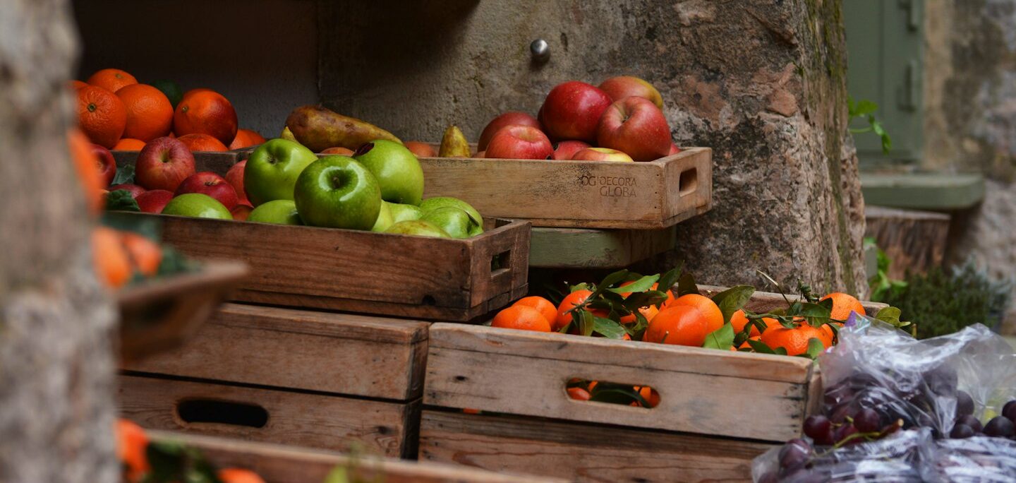 Frutta fresca in cassette di legno sotto scaffali di olio d'oliva.